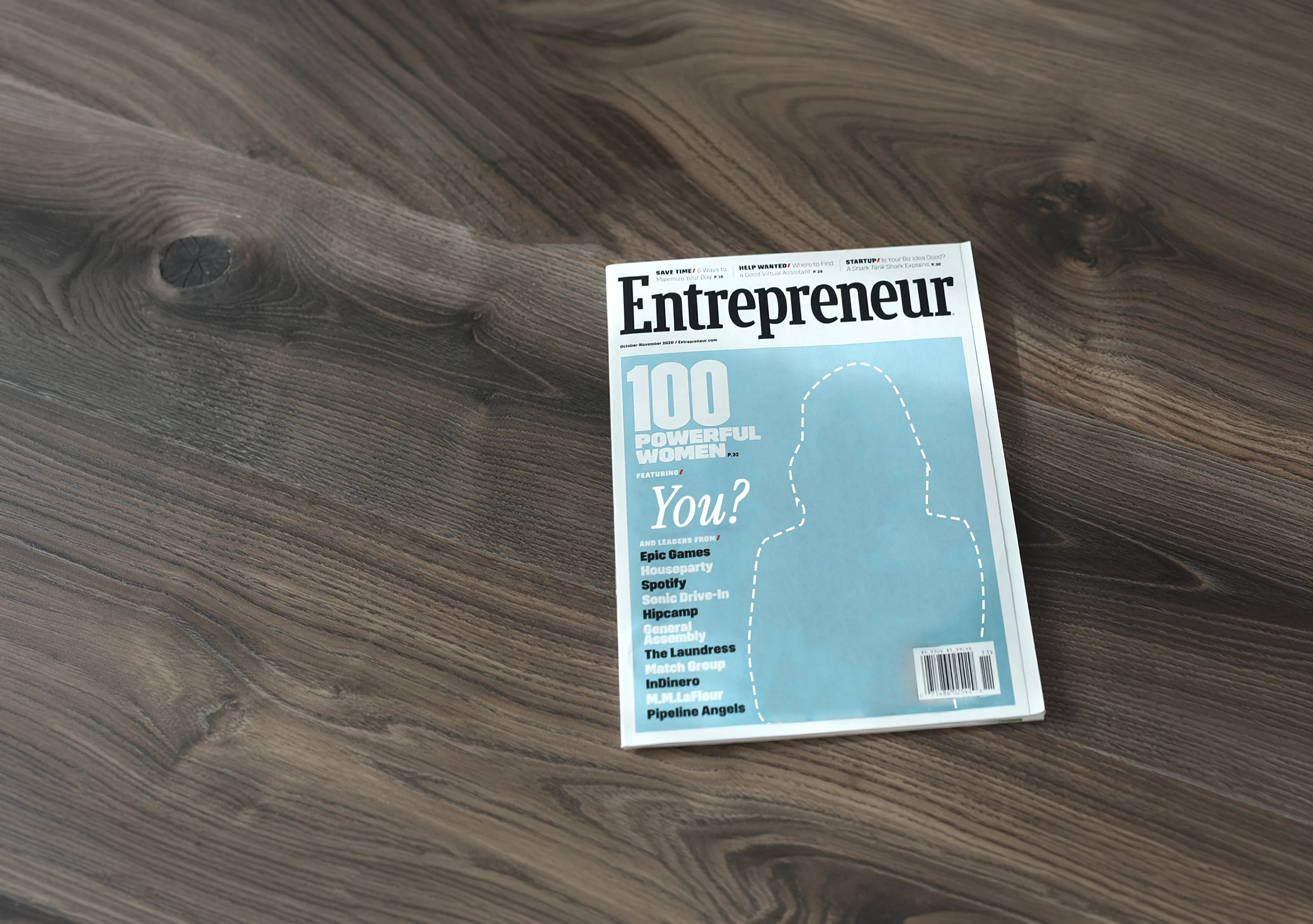 Entrepreneur magazine on a dark oak desk: its 100 Powerful Women cover reads “featuring You?” over an empty silhouette