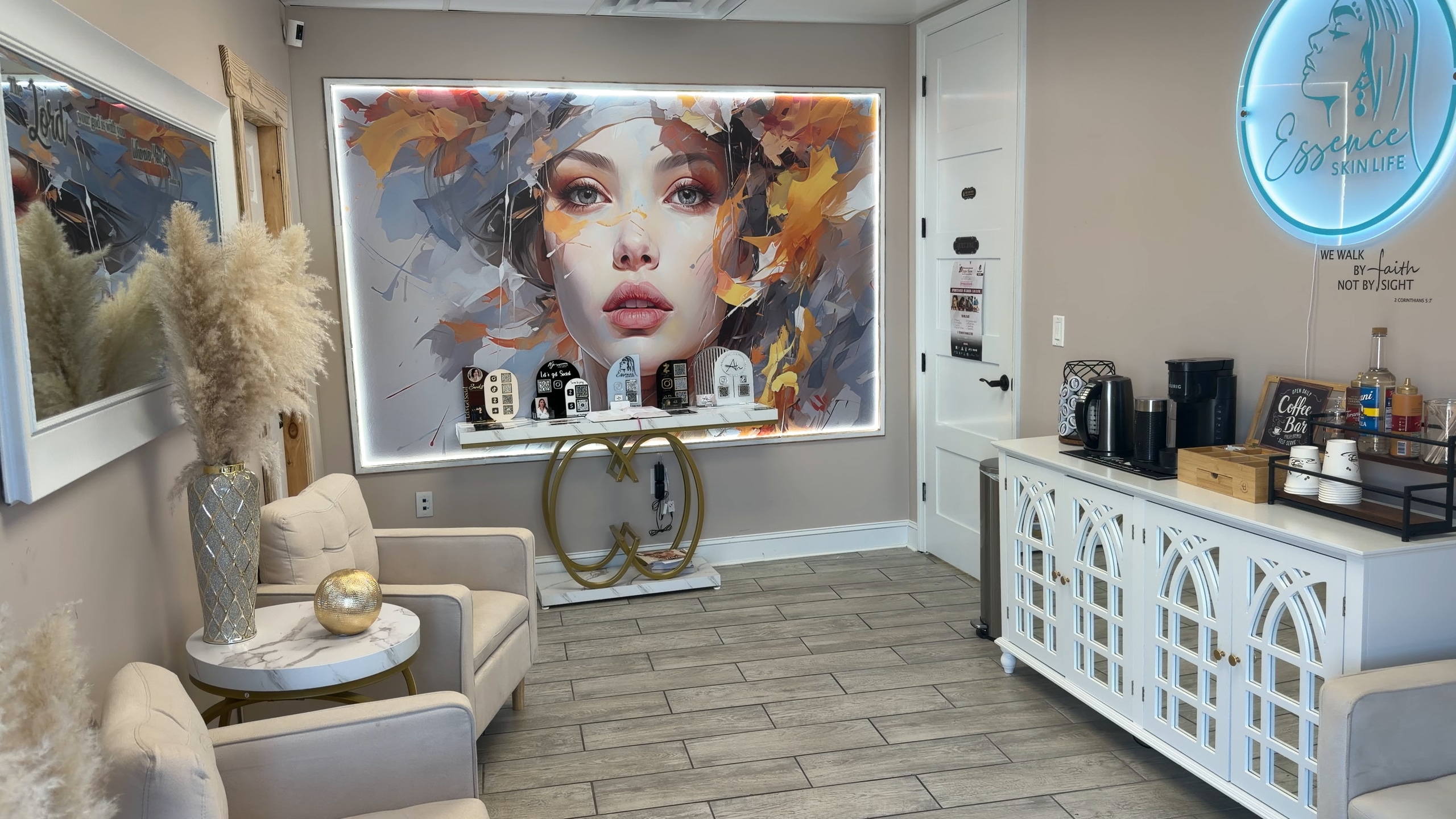 The Essence waiting room: a large backlit painting of a face over a gold console, cream armchairs and the coffee cabinet